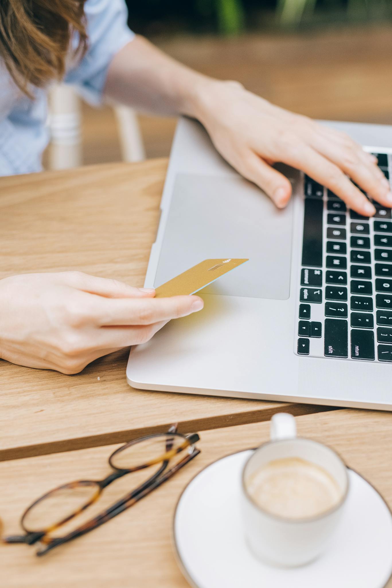 Woman making an online purchase using a credit card and laptop on a wooden table.